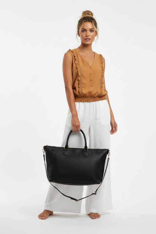 Studio shot - model with hair up wearing rust top, white pants, and black tote bag